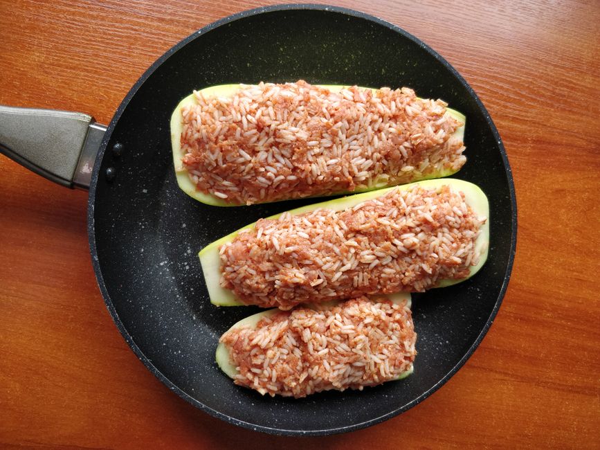 Appetizing stuffed zucchini with rice, served in a skillet on a wooden table.